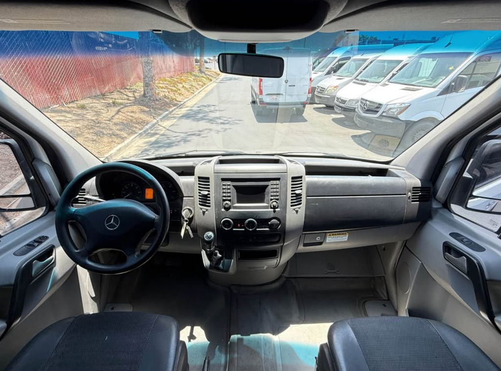 Car interior with dashboard and steering wheel, showing a view of a parking lot.